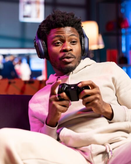 Jovem segura controle e joga videogame sentado no sofá.