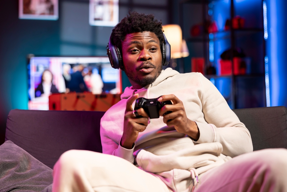 Jovem segura controle e joga videogame sentado no sofá.