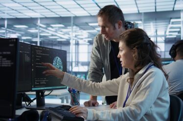 Profissionais de TI observam informações me monitor enquanto um deles aponta para a tela.