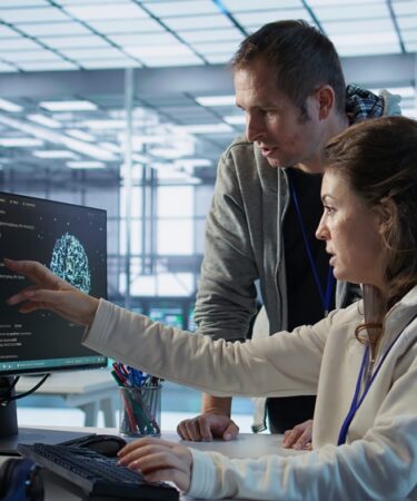 Profissionais de TI observam informações me monitor enquanto um deles aponta para a tela.