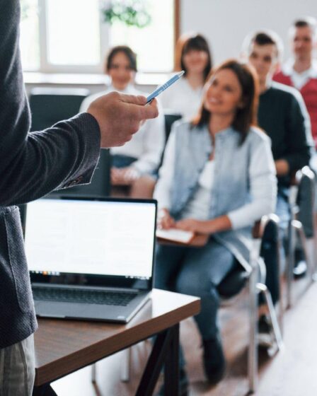 Professor palestrante em sala de aula com alunos atentos, simulando uma defesa de tese ou aula de doutorado e mestrado.