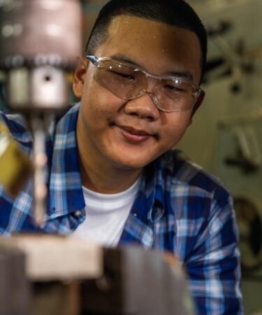 Profissional jovem com óculos de proteção enquanto se concentra na execução de um trabalho com máquina industrial.