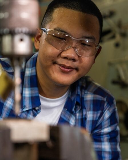 Profissional jovem com óculos de proteção enquanto se concentra na execução de um trabalho com máquina industrial.