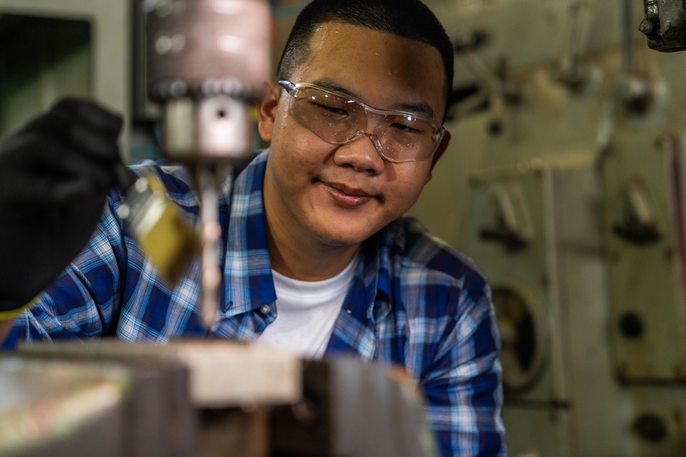 Profissional jovem com óculos de proteção enquanto se concentra na execução de um trabalho com máquina industrial.