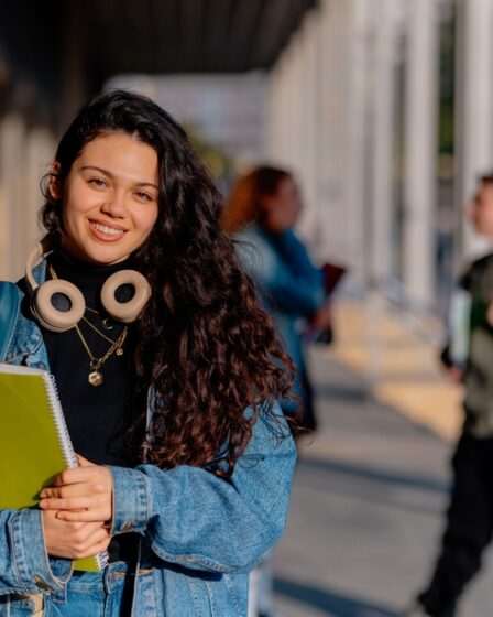 Estudante universitária sorridente segurando cadernos de anotações, curtindo seu retorno à escola enquanto abraça a atmosfera vibrante do campus