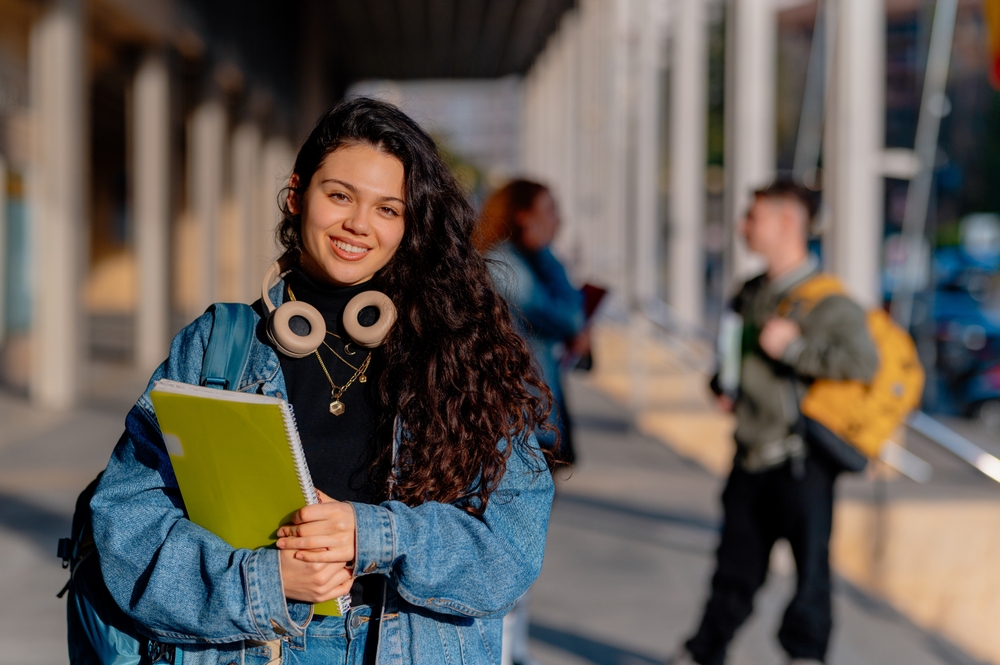 Estudante universitária sorridente segurando cadernos de anotações, curtindo seu retorno à escola enquanto abraça a atmosfera vibrante do campus