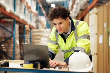 homem agachado mexe em um laptop em um deposito.