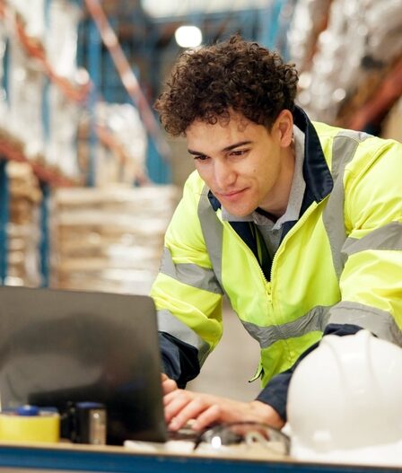 homem agachado mexe em um laptop em um deposito.