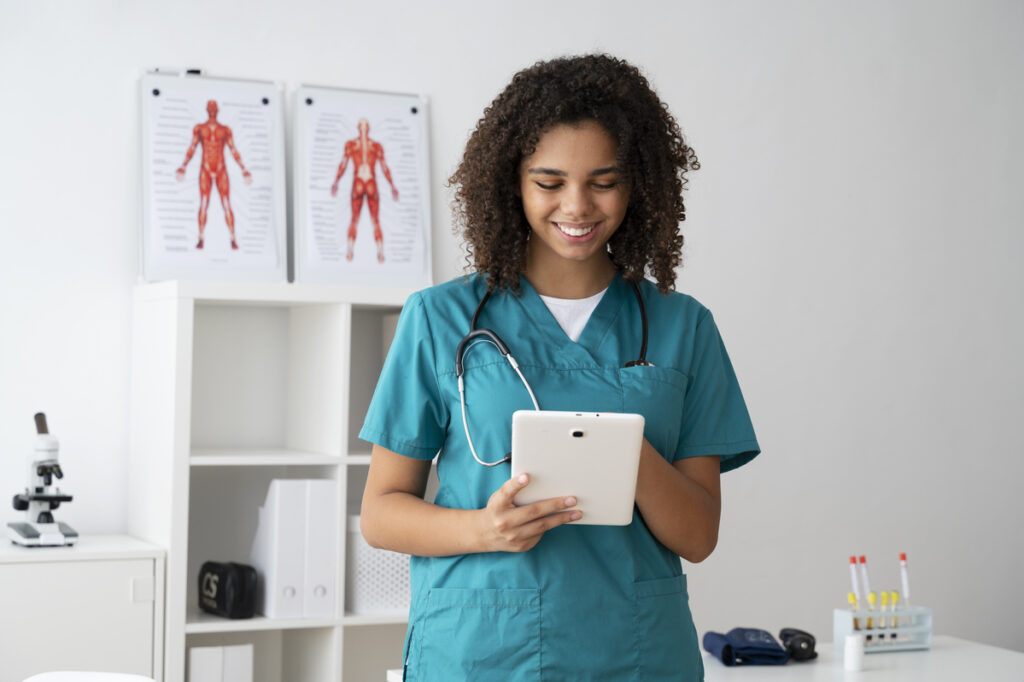 Técnica de enfermagem utilizando um tablet para registrar informações de pacientes em consultório médico equipado com materiais clínicos.