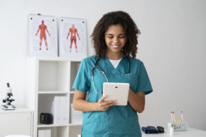 Técnica de enfermagem utilizando um tablet para registrar informações de pacientes em consultório médico equipado com materiais clínicos.