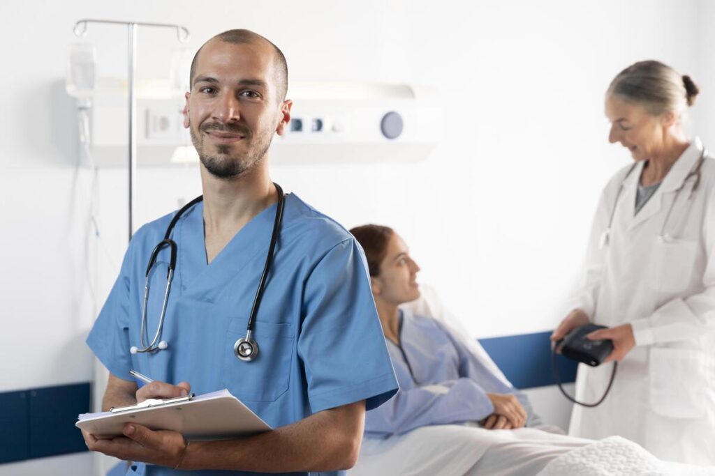Técnico de enfermagem segurando uma prancheta durante atendimento hospitalar, enquanto médica acompanha uma paciente internada ao fundo.
