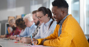 Pessoas multiétnicas sentadas à mesa, fazendo anotações, participando de um seminário de consultoria. Adultos de diferentes origens estudando em sala de aula em cursos de pós-graduação na faculdade.