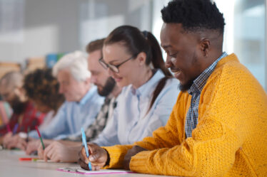 Pessoas multiétnicas sentadas à mesa, fazendo anotações, participando de um seminário de consultoria. Adultos de diferentes origens estudando em sala de aula em cursos de pós-graduação na faculdade.