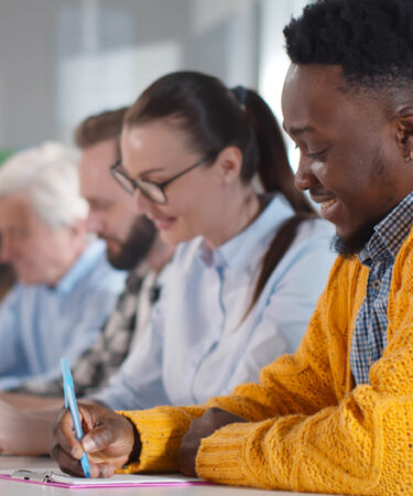 Pessoas multiétnicas sentadas à mesa, fazendo anotações, participando de um seminário de consultoria. Adultos de diferentes origens estudando em sala de aula em cursos de pós-graduação na faculdade.