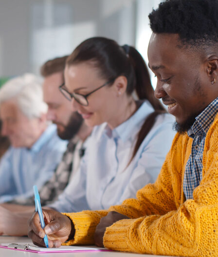 Pessoas multiétnicas sentadas à mesa, fazendo anotações, participando de um seminário de consultoria. Adultos de diferentes origens estudando em sala de aula em cursos de pós-graduação na faculdade.