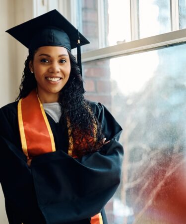 Estudante afro-americana de pós-graduação, feliz, em pé com os braços cruzados e olhando para a câmera.