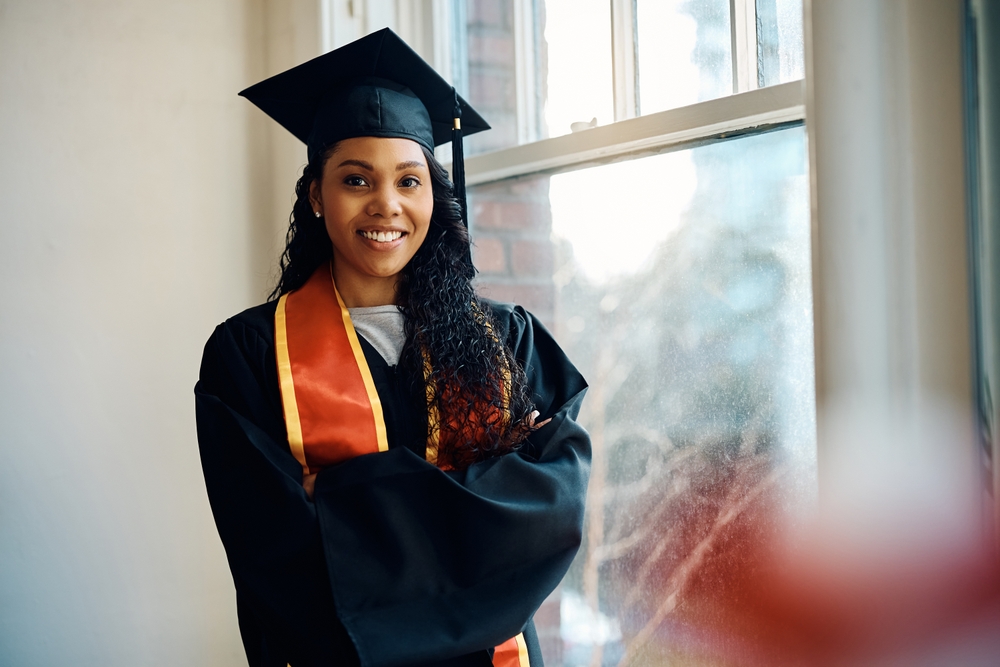 Estudante afro-americana de pós-graduação, feliz, em pé com os braços cruzados e olhando para a câmera.