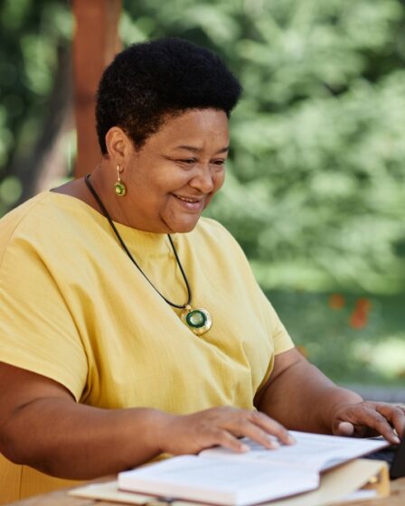 Mulher negra idosa usando laptop ao ar livre em uma mesa de café e sorrindo.