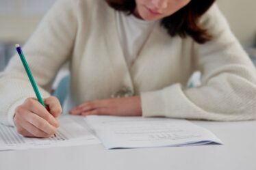 Menina sentada preenche o gabarito de uma prova com lápis.