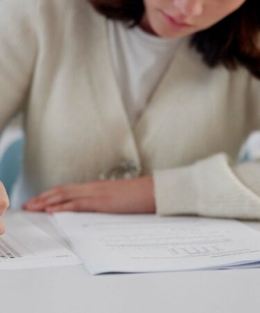 Menina sentada preenche o gabarito de uma prova com lápis.