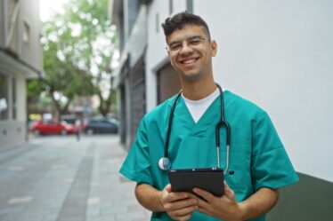 Jovem técnico de enfermagem sorrindo vestindo uniforme e estetoscópio.