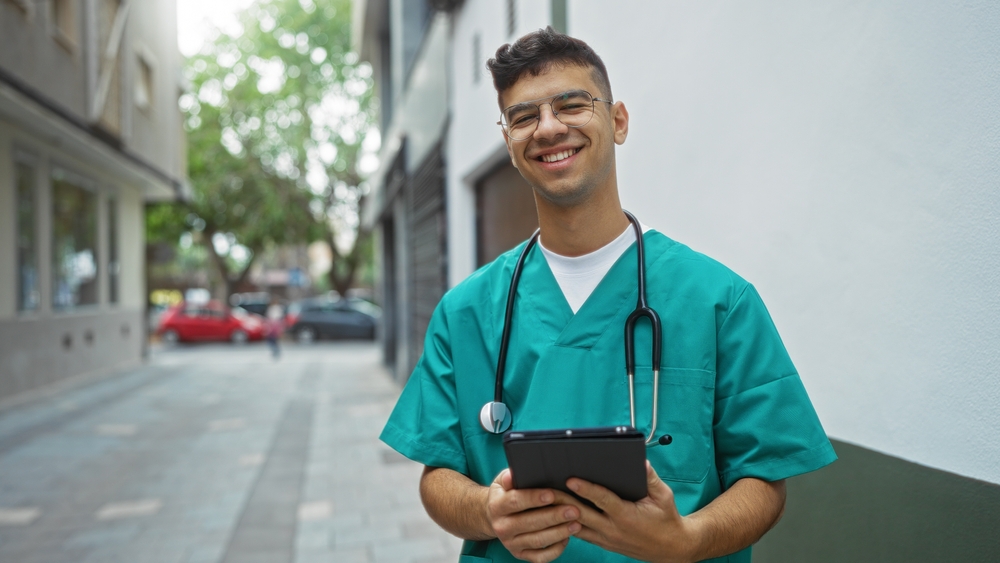 Jovem técnico de enfermagem sorrindo vestindo uniforme e estetoscópio.
