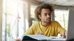Homem jovem usando notebook e material de apoio, pesquisando sobre cursos técnicos mais valorizados para ingressar no mercado de trabalho.
