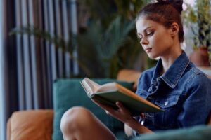 Mulher jovem de cabelo castanho e pele branca lê um livro de capa verde de maneira concentrada.