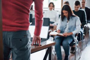 Professor em pé conduzindo avaliação enquanto alunos realizam prova em sala de aula, ilustrando o contexto de o que é Enade e sua aplicação no ensino superior.