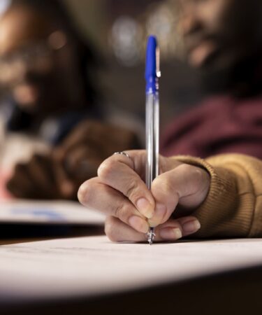 Close nas mãos de estudante escrevendo em folha de prova durante avaliação acadêmica, representando o que é Enade e o momento de realização do exame.