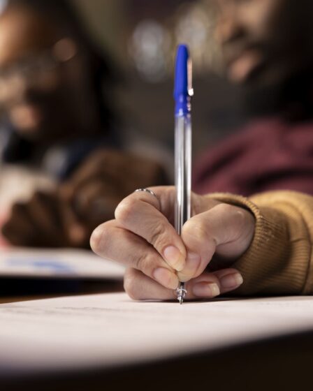 Close nas mãos de estudante escrevendo em folha de prova durante avaliação acadêmica, representando o que é Enade e o momento de realização do exame.