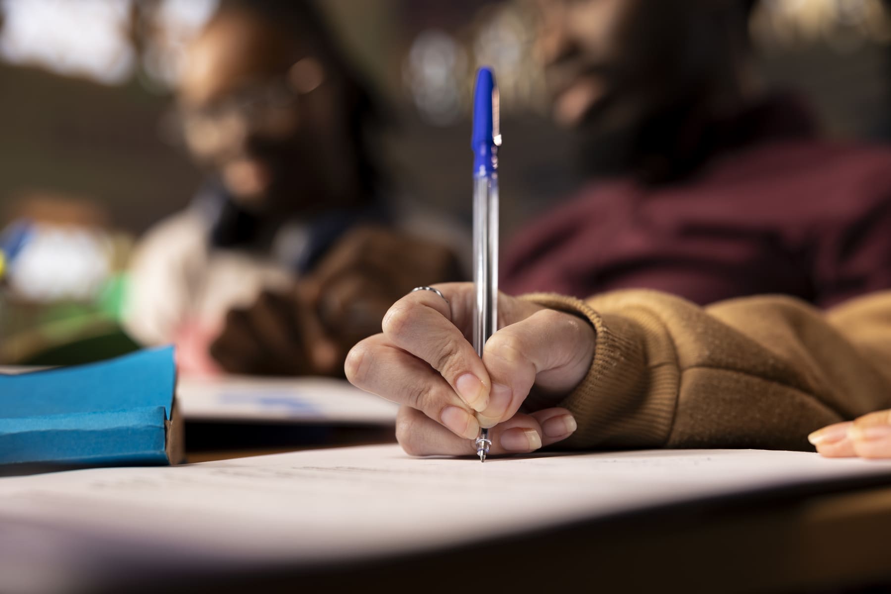 Close nas mãos de estudante escrevendo em folha de prova durante avaliação acadêmica, representando o que é Enade e o momento de realização do exame.