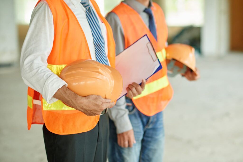 Profissionais com coletes refletivos e capacetes nas mãos em ambiente corporativo, representando a Segurança do Trabalho.