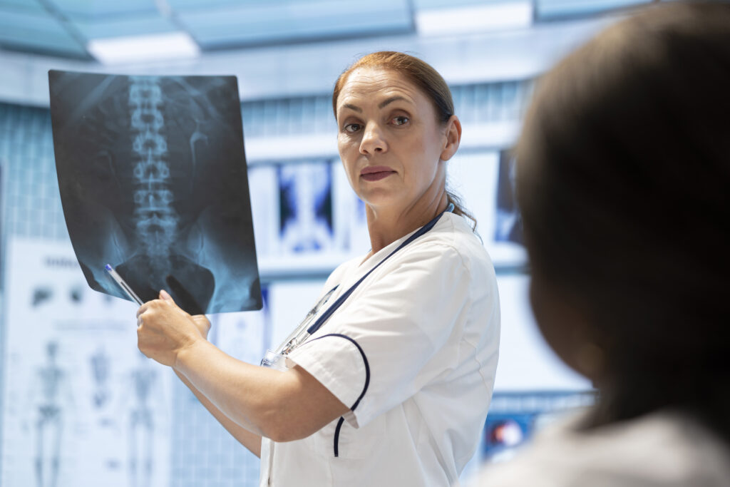 Profissional de saúde explicando um exame de coluna em raio-x para paciente, ilustrando a prática clínica ensinada em um curso de Radiologia.