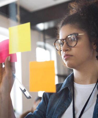 Jovem organizando post-its em um quadro durante planejamento estratégico, ilustrando o que é PDI para o desenvolvimento acadêmico.