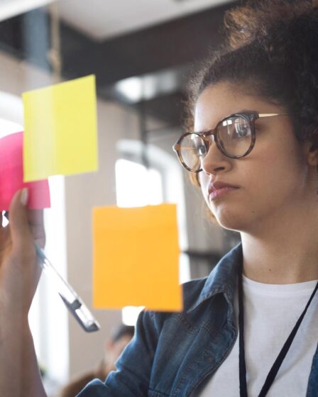 Jovem organizando post-its em um quadro durante planejamento estratégico, ilustrando o que é PDI para o desenvolvimento acadêmico.