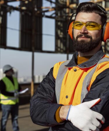 Profissional com EPI completo, incluindo óculos e protetor auricular, em obra, simbolizando a Segurança do Trabalho.