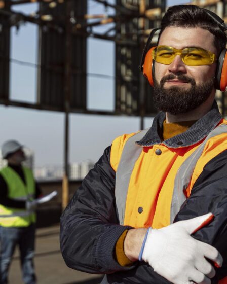 Profissional com EPI completo, incluindo óculos e protetor auricular, em obra, simbolizando a Segurança do Trabalho.