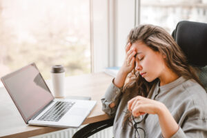 Mulher cansada em frente ao notebook, com expressão de fadiga e sobrecarga durante o trabalho.