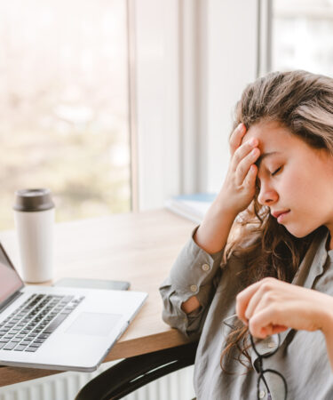 Mulher cansada em frente ao notebook, com expressão de fadiga e sobrecarga durante o trabalho.