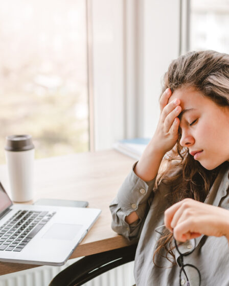 Mulher cansada em frente ao notebook, com expressão de fadiga e sobrecarga durante o trabalho.