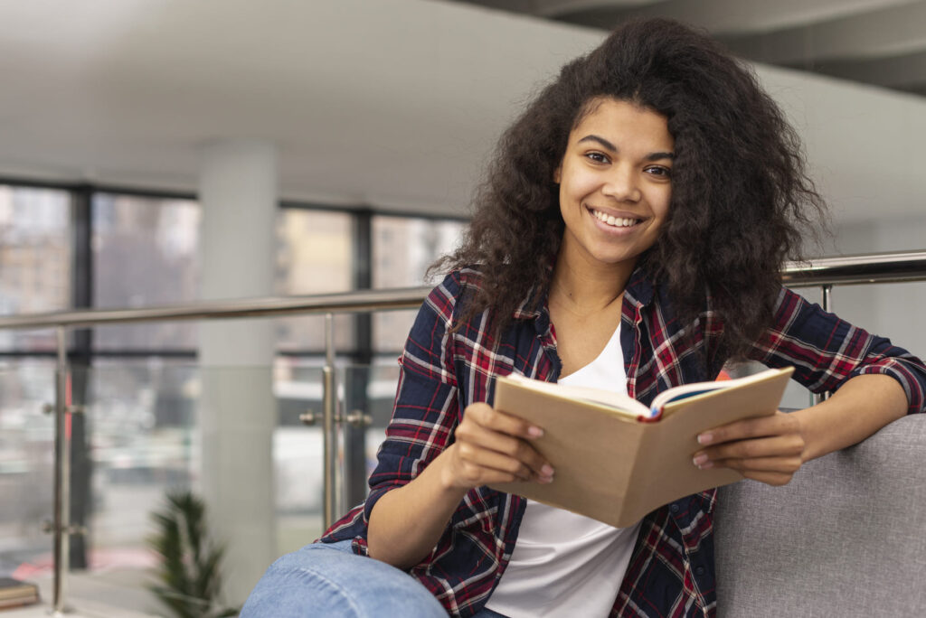 Jovem estudante sorrindo enquanto lê um livro em ambiente universitário, pesquisando como funciona o Prouni.