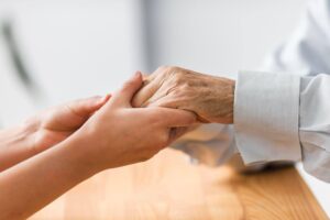 Mãos de cuidador segurando mãos de idoso em gesto de apoio, simbolizando o que é Gerontologia e o cuidado humanizado na terceira idade.