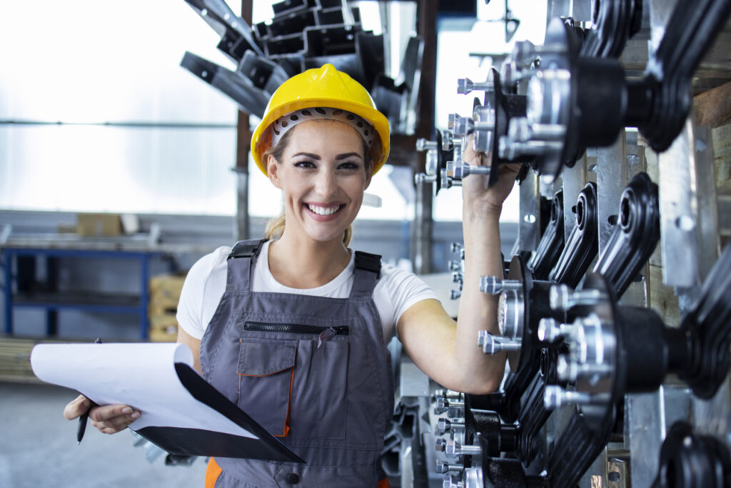 Mulher engenheira com capacete amarelo analisando equipamentos industriais em fábrica, representando atividades práticas da faculdade de Engenharia Mecânica.