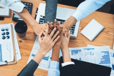 Membros de equipe profissional unem as mãos sobre uma mesa de escritório no trabalho.