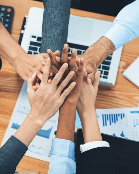 Membros de equipe profissional unem as mãos sobre uma mesa de escritório no trabalho.