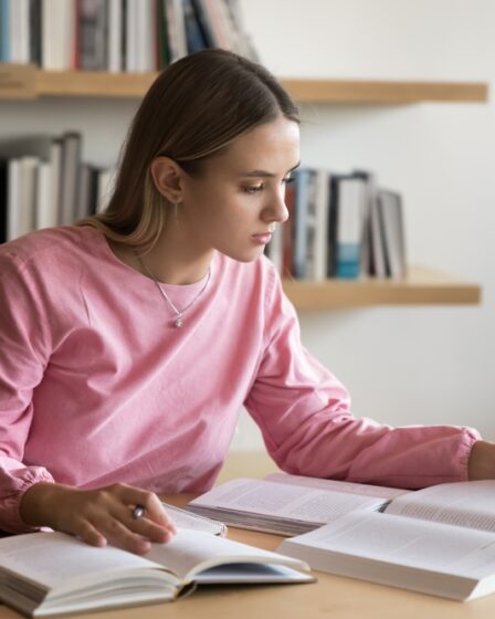 Mulher estudante concentrada lendo e fazendo anotações em ambiente de estudo.