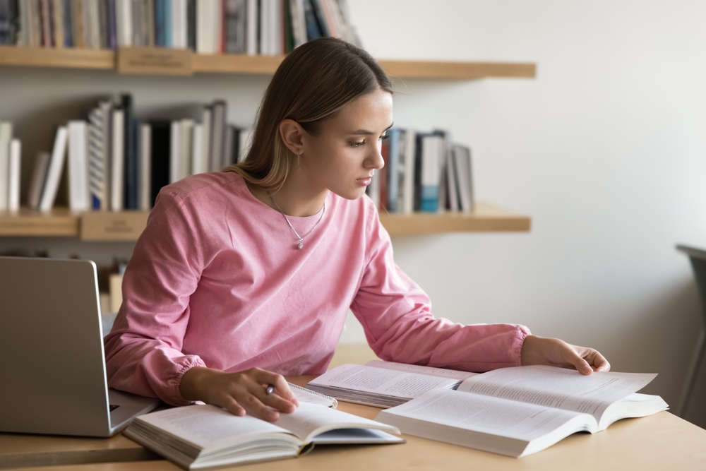 Mulher estudante concentrada lendo e fazendo anotações em ambiente de estudo.