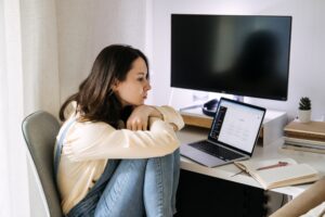 Mulher jovem sentada com o corpo encolhido, reflexiva, em frente ao notebook na tela de inteligência artificial. 