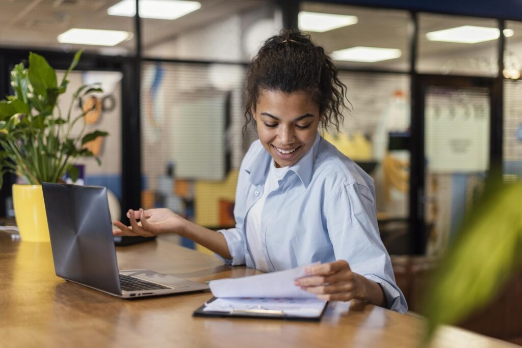 Jovem analisando documentos ao lado do notebook, demonstrando organização e foco, exemplo de o que é proatividade no dia a dia